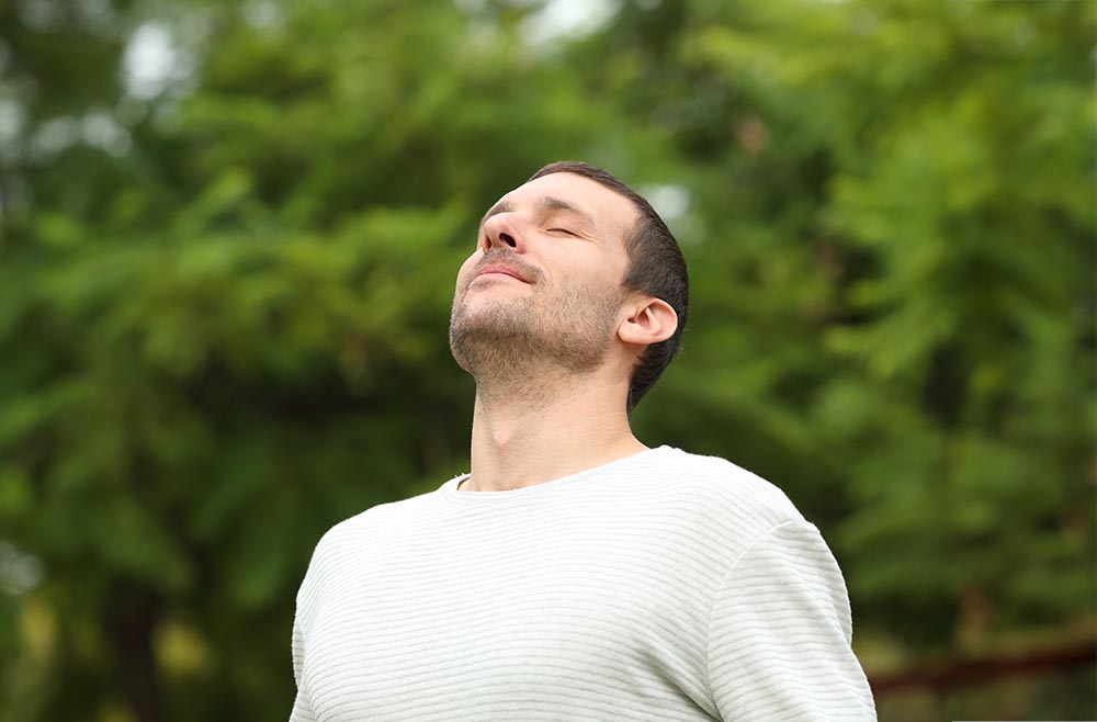 Relaxed adult man breathing fresh air in a forest with green trees in the background